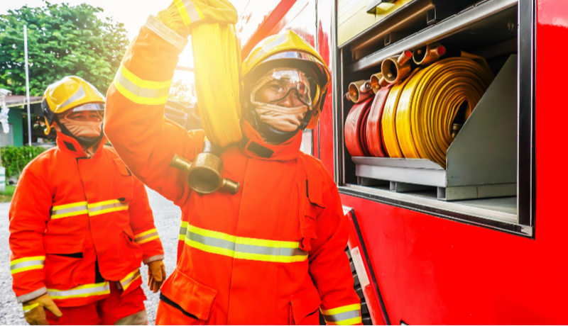 Two fire and rescue officer in uniform stood next to a fire engine, one is holding a fire house