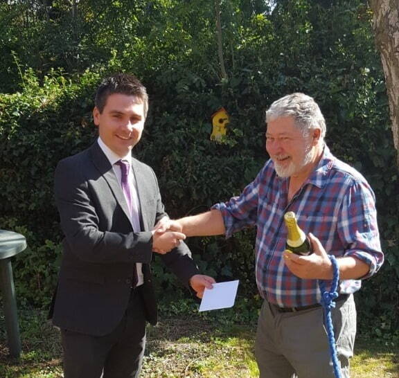 A young man gives an older gentleman a bottle of champagne